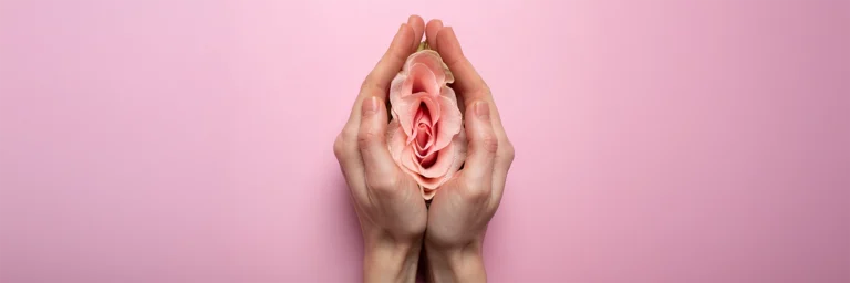Mano femeninas tomando una flor sobre fondo rosado