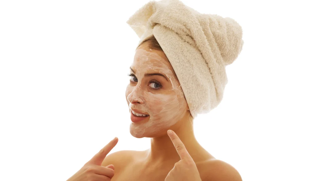 Mujer joven con toalla en la cabeza aplicando un exfoliante blanco en su rostro
